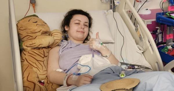 Imali lying in a hospital bed giving a thumbs up with one hand